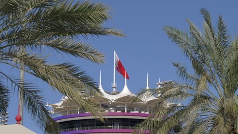 View Through Palm Trees Of Bahraini Flag On Sakhir Tower. Bahrain International Circuit In Manama, Kingdom Of Bahrain. medium shot, slow motion