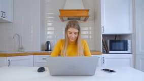 Working from home on lockdown. Young adult woman doing distant work on laptop in kitchen. Beautiful white female studying online with notebook pc and internet connection. Freelancer person video in 4k