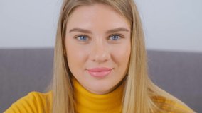 Beautiful blonde woman looking in camera with cheerful smile. Attractive white female with long blond hair and pink lips posing for 4k stock video. Cute young adult person wearing mustard yellow shirt