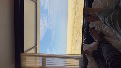 Vertical video. Young couple laying in bed. Man and woman barefoot, naked legs and feet on linen relaxing. Panoramic view at field with dried yellow grass. Savannah in Africa. Vacation honeymoon.