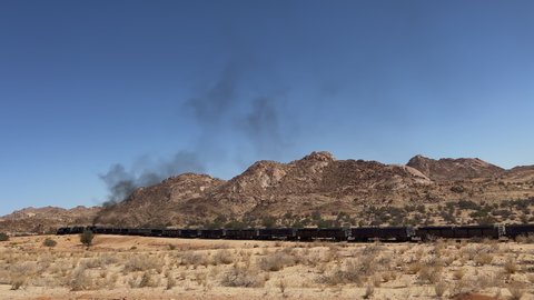 Freight train rides on the railroad in the desert. Locomotive and wagons. Desert sandy landscape and mountains in Africa, Namibia. Railway cargo transportation. American wild west, Arizona.