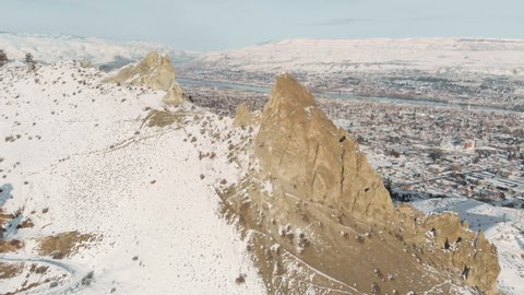 4K drone video of rugged rock spire with river and city in the snow covered valley below in Wenatchee, Washington