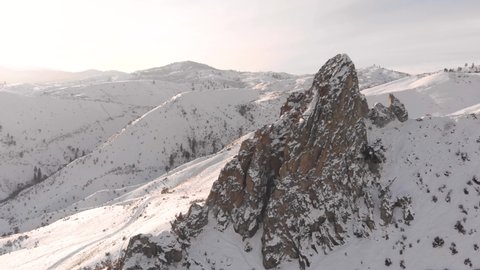 4K drone video of wrapping around a rock pinnacle in the snow and hills in the Pacific Northwest