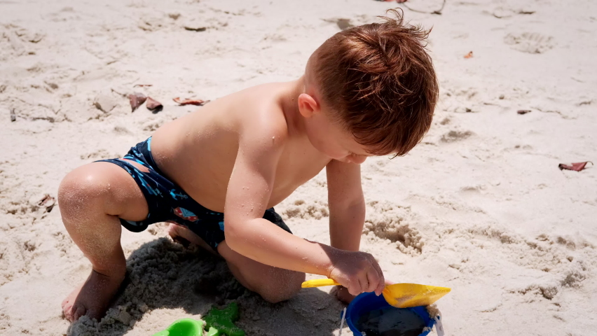 Little boy playing with sand on beach ocean sea and building sand castle house.