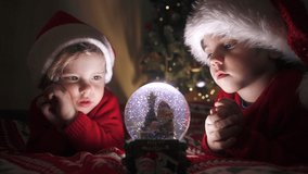 Cute little boys in Santa hats with snow globe. New Year's gift toy for children. Magic Christmas time, toddlers look at glass ball with interest. Family, brothers, holidays and celebration concept - Powered by Shutterstock - Get 15% off with code: PIKWIZARD15
