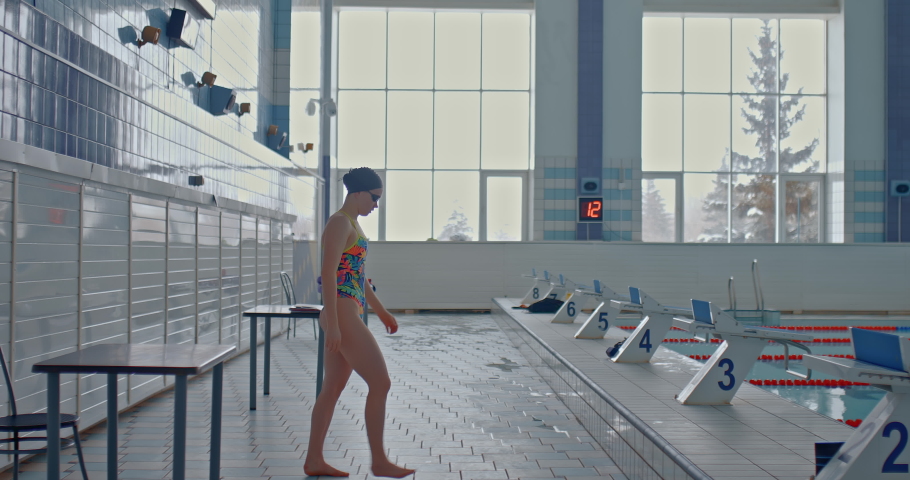 Swimmer girl approaches the diving stand and stands in a rack. Professional swimmer prepares for a jump, stands in a stand for jumping on a springboard. Beginning of the distance in swimming Royalty-Free Stock Footage #1085766449