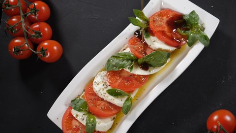 Chef pouring olive oil over caprese salad. Slow motion. Healthy and vegetarian food. Top view. Traditional Italian caprese salad with Mozzarella cheese and tomatoes. Full hd
