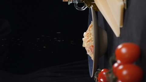 Serving pasta in restaurant on black background. Dry spices falling on freshly cooked seafood pasta. Slow motion. Vertical footage. Tasty Italian food. Full hd