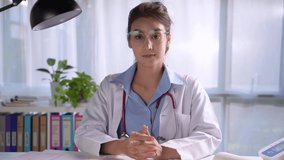 Young beautiful Asian female doctor looking at camera in medical office, having online consultation with patient. Young female doctor with stethoscope making video call