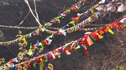 Slow motion shot of colorful Buddhist Tibetan prayer flag in front of mountains at Pangan Nyingmapa Monastery in Patlikuhal village near Manali, Himachal Pradesh, India