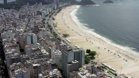 Aerial view of Copacabana Brazil. Life is a beach on the ocean, with sand, umbrellas and waves bordering the skyscrapers on the roads on which transport travels.