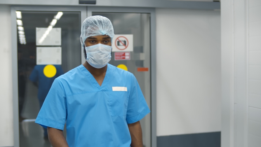 Portrait of tired surgeon removing safety cap and mask walking in hallway after long surgery. Exhausted male doctor walking in hospital corridor Royalty-Free Stock Footage #1085780846
