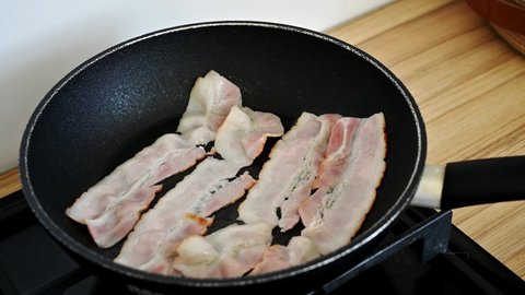Closeup of bacon strips frying in a non stick pan in a home kitchen preparing a keto breakfast or meal