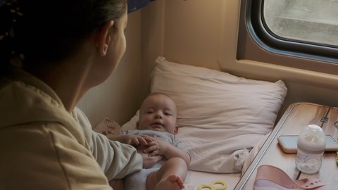 Mom and son travelling by train, long-distance family trip by railway in train compartment, cute 6 months old toddler lying on seat by window. High quality 4k footage