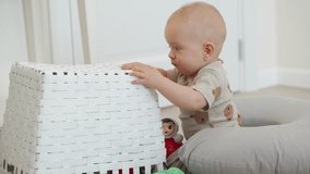 Baby sitting on the floor inspecting a white toy box playing with toys, cute little baby boy having fun exploring new world. High quality 4k footage