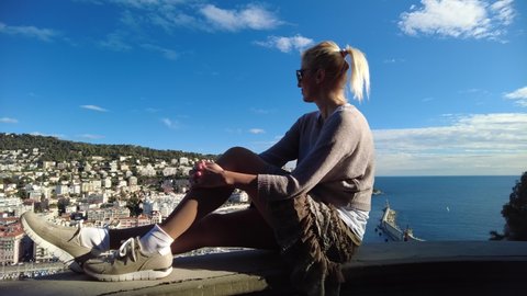 woman sitting on top rooftop view of panorama of the Nice city and Port Lympia in Blue Coast of France. Aerial view of cityscape with lighthouse from the panoramic terrace of Colline du Chateau park.