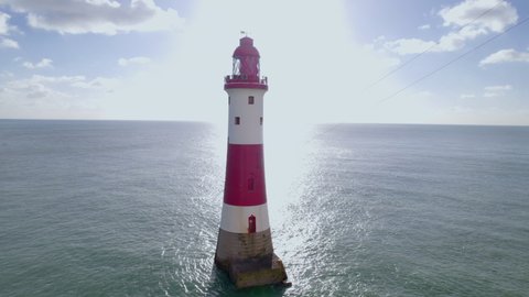 Aerial shot circling around lighthouse in bright sun with high white cliffs, Beachy Head, UK