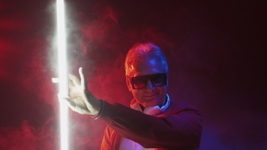 Excited dance. Funky man. Weekend night. Neon party. Happy carefree senior male having fun enjoying nightclub music in glowing colorful light smoke flow.
