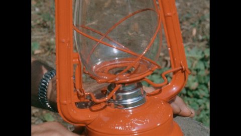 1960s: Hand holds metal lighter. Thumb spins sparkwheel and lighter flames. Kerosene lamp is lit with match.