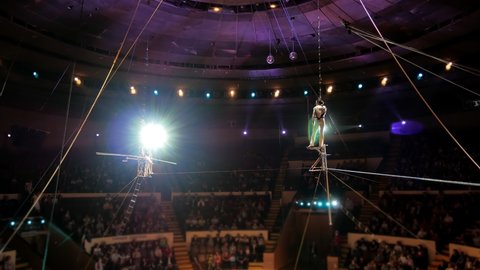 Performance of three aerial tightrope walkers gymnasts in white suits in the circus. Aerialists arrange a show for the audience under the dome of the circus, a tightrope walker walks on a rope.