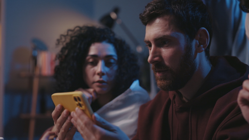 Close up of joyed multiethnic people screaming while watching results of the game on smartphone and sitting on sofa. Focus on bearded guy rejoicing together with friends and screaming Royalty-Free Stock Footage #1085793101