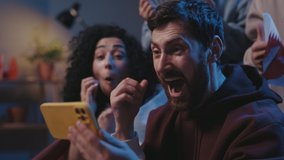 Close up of joyed multiethnic people screaming while watching results of the game on smartphone and sitting on sofa. Focus on bearded guy rejoicing together with friends and screaming - Powered by Shutterstock - Get 15% off with code: PIKWIZARD15