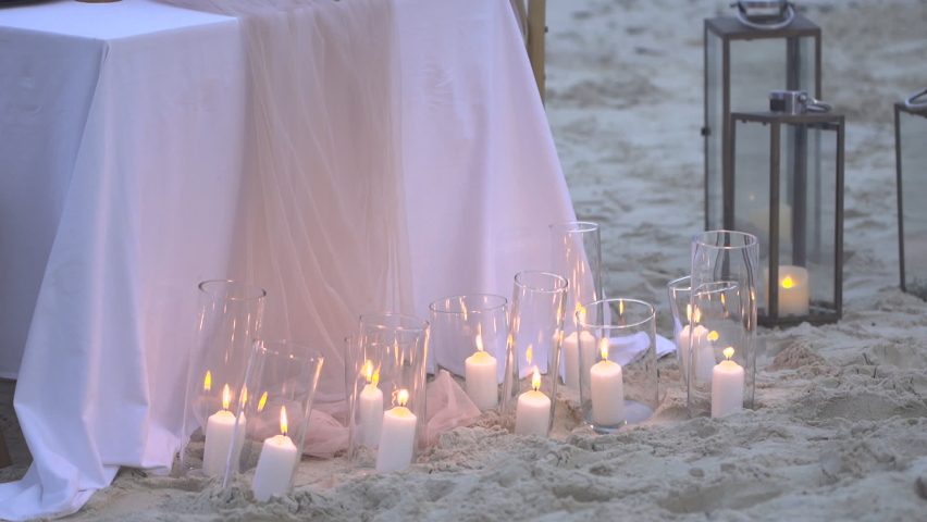 Candlelight bright decoration on sandy beach during sunset. Romantic setting table dinner. Sunset beach dinner table on wedding anniversary | Shutterstock HD Video #1085793686