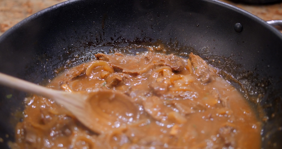 Close up of huge wok while cooking sauteed beef stew with onions, soy sauce and coriander in a light brown sauce.