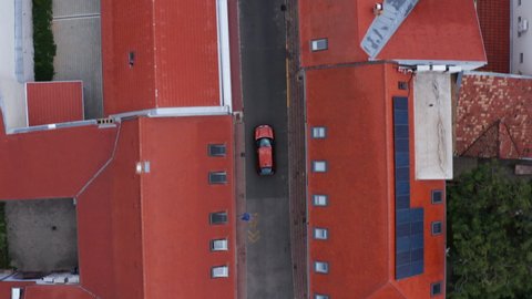 Top View Of Orange Car Driving In The Street Between Red Roofed Buildings In Pecs, Hungary. - aerial