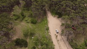 Four wheel white vehicle driving on unpaved road in forest at Mar de las Pampas in Argentina. Aerial tilt-up reveal