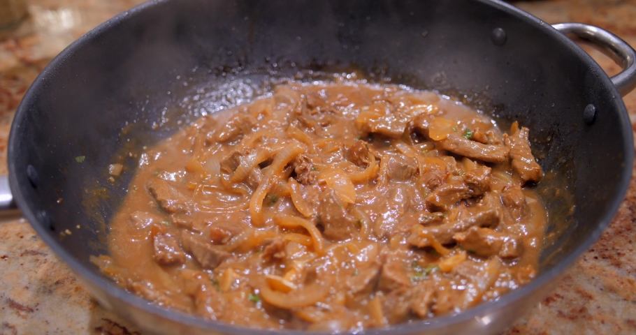 Lid covering and uncovering wok while cooking sauteed beef stew with onions, soy sauce and coriander in a light brown sauce.
