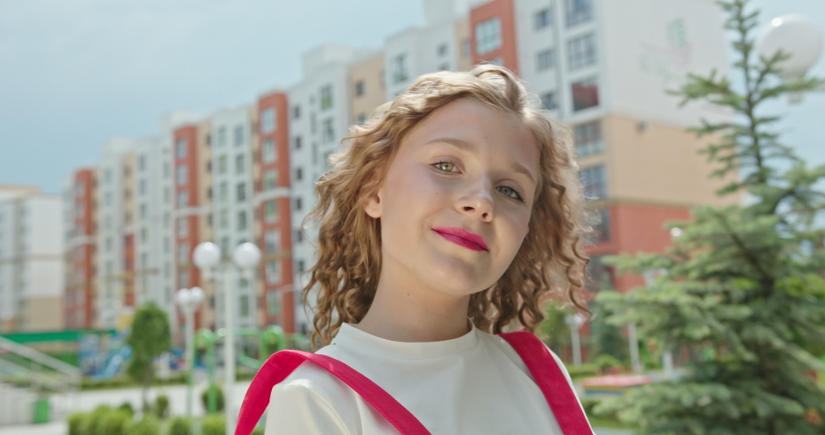 Beautiful little girl with blond curly hair smiles, shakes her head in bright pink clothes and poses for the camera on the background of the newest residential complexes | Shutterstock HD Video #1085797037