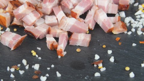 Meat delicacy. Sliced bacon cubes, basil and seasonings on a rotating slate tray. Macro