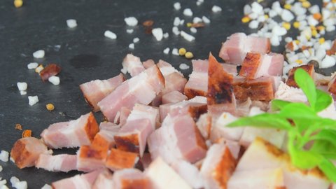 Dice bacon, basil and seasonings on rotating slate tray. Sliced bacon cubes, basil and seasonings on a rotating slate plate. Macro