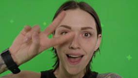 Young smiling woman posing on green screen background. Girl taking selfie self portrait photo on smartphone. Chroma key. Female model showing positive face emotions. 4k raw video footage