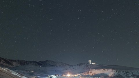Timelapse of the night sky over snowy mountain landscape with moving radio telescope, Sierra Nevada, Spain