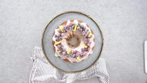 Flat lay. Step by step. Slicing lemon cranberry bundt cake decorated with sugar cranberries and lemon wedges.
