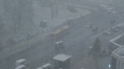 Top view of city street in heavy snowfall. Public transport, cars move along street. Poor visibility. People are hiding from snowstorm under canopy, passers-by walking along sidewalks, slow motion.