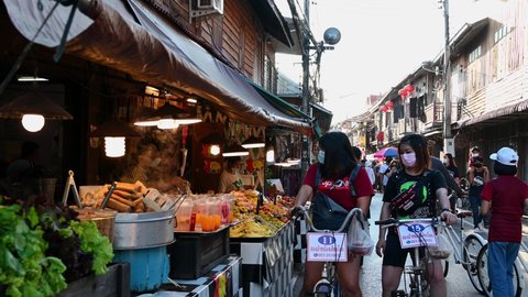 Chiang Khan , Loei , Thailand - 01 01 2022: Two ladies on their bicycles stopping to buy some street Thai food along the Walking Street, Chiang Khan in Loei, Thailand.