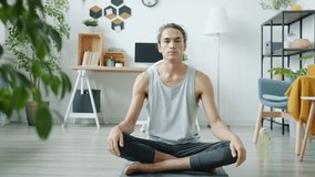 Portrait of young man teaching yoga online speaking and demonstrating exercise from home. Vlogging and social media tutorials concept.