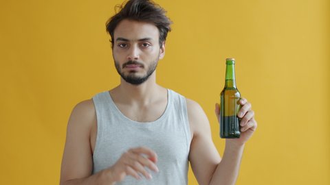 Young Arab sportsman looking at beer bottle then saying no avoiding alcohol on yellow background. Healthy lifestyle and active youth concept.