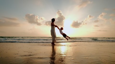 Happy mother and son playing on the beach at sunset
