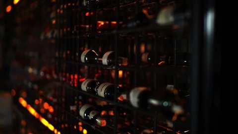 Bottles of wine stands in a dark cellar. Wine factory. Exhibition stand, rack bottles with alcohol. Soft focused footage.