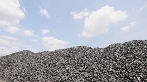 Coke coal in the warehouse. A mountain of coke oven coal against the background of the time lapse sky. Coal in stock