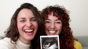 POV LGBT lesbian couple doing video call holding ultrasound photo scan of growing baby in pregnancy time - Powered by Shutterstock - Get 15% off with code: PIKWIZARD15