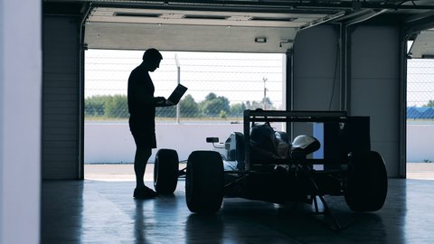 A mechanic with a laptop is checking a racing car