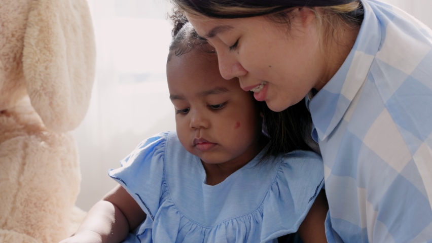 Mother and african american daughter watching content on smartphones or tablet. Happy family parents and little children enjoy using devices together sit on the floor at home. slow motion
