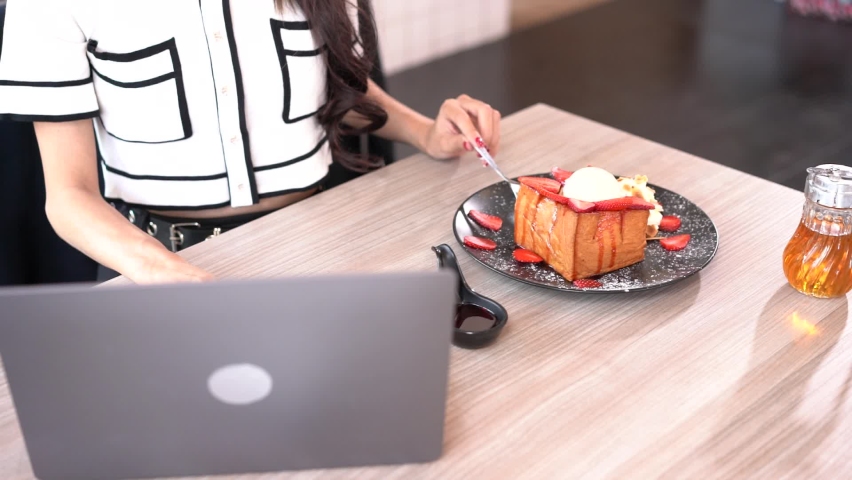 Working woman eating dessert, Honey toast with ice cream and working on grey laptop in coffee shop. Female enjoy life work outside company as remote working.