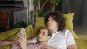 Male romantic gay couple relaxing on the couch, watching the smartphone screen