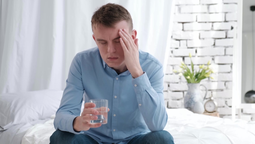 Man with headache drinking water while sitting on bed at home. Concept: hangover, headache | Shutterstock HD Video #1085834087